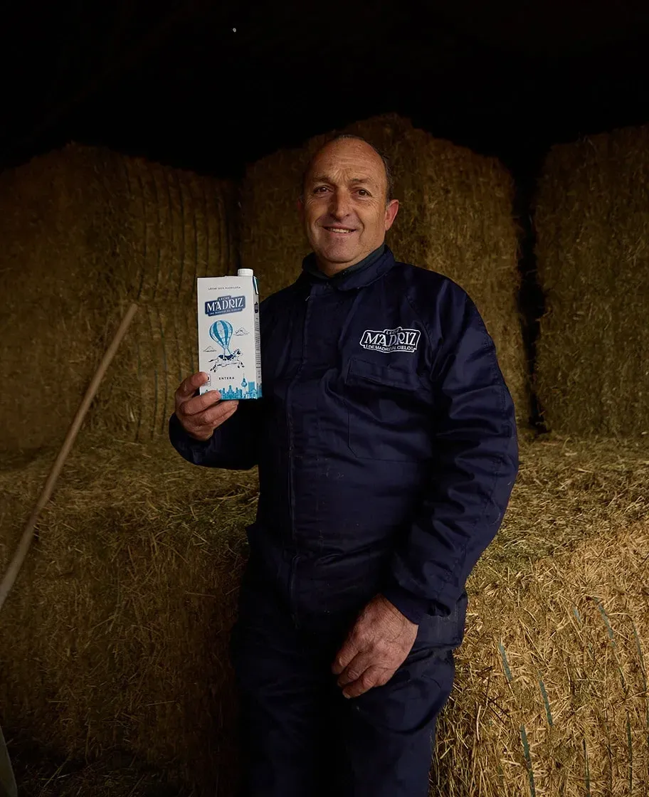 Un ganadero de Leche Madriz con un brik en la mano, delante de las balas de paja